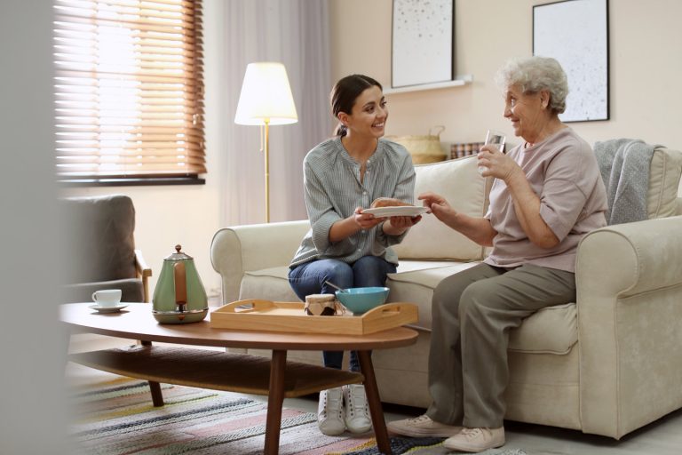 Young caregiver serving dinner for elderly alzheimer's woman in living room