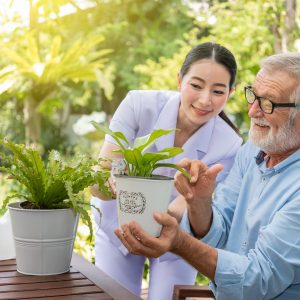 Caregiver help assist senior man watering plants